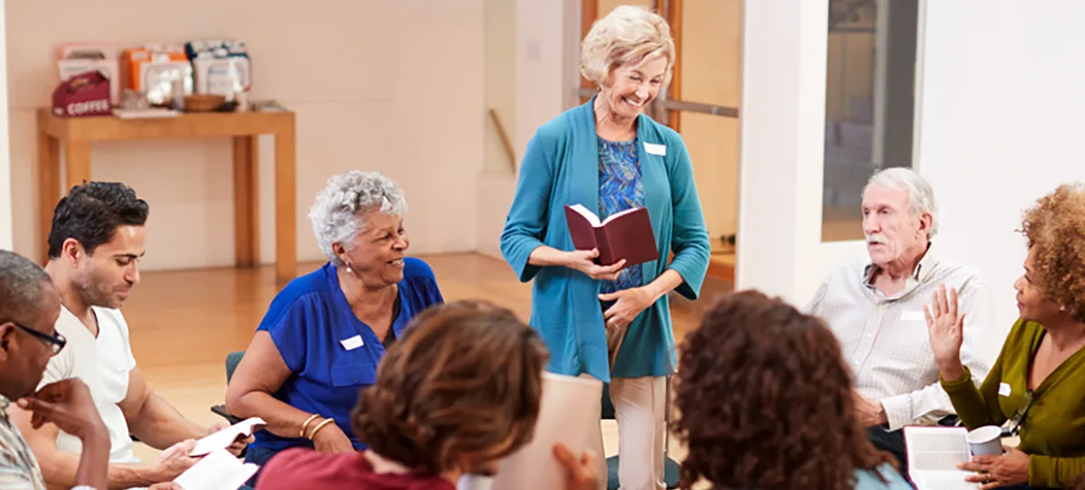 older woman standing and reading to group of people