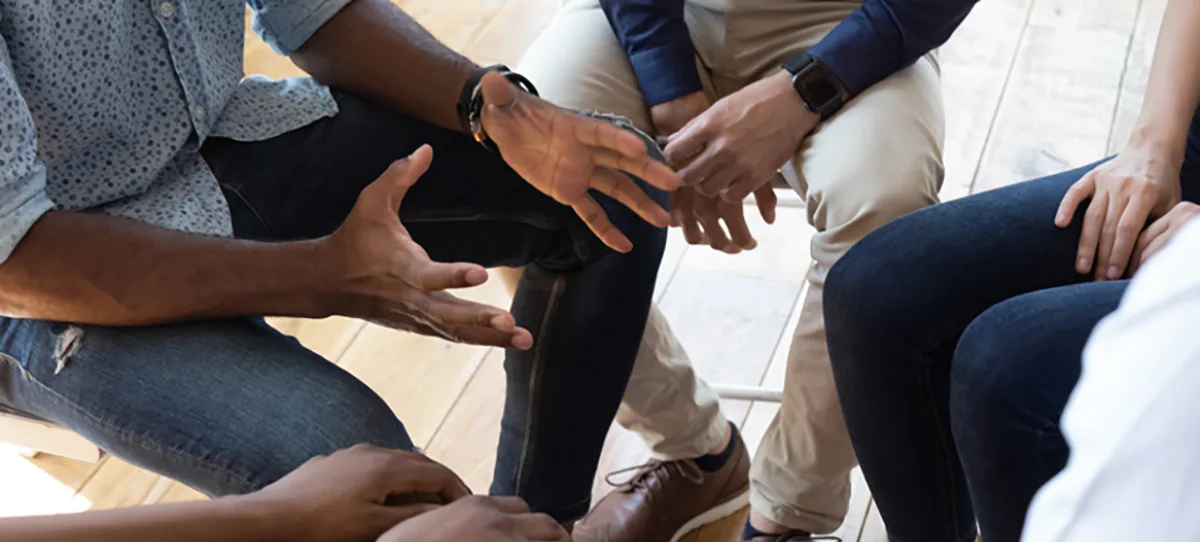 photo of people talking while seated in a circle zoomed in to their hands and legs